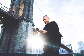 Smiling shapely male using mobile near bridge