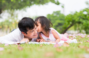 Asian father and daughter are lying and kissing together on the green lawn and flowers and the...