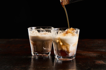 coffee liquor poring in glasses with ice cubes isolated on black