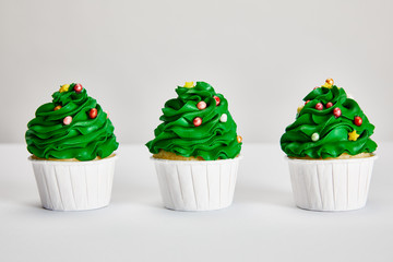 Obraz na płótnie Canvas tasty Christmas tree cupcakes in row on white surface isolated on grey