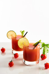 bloody mary cocktail in glasses garnished with lime and celery isolated on white with tomatoes