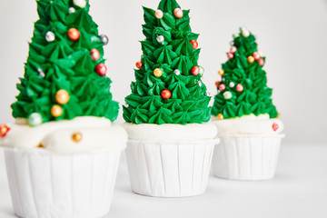 selective focus of delicious Christmas tree cupcakes in row on white surface isolated on grey