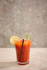 bloody mary cocktail in glass with lime, celery and straw on grey background