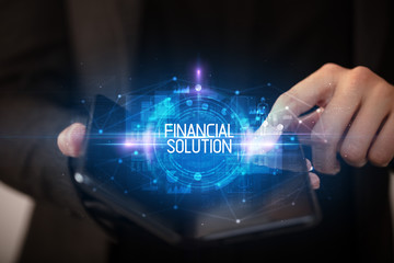 Naklejka premium Young man holding a foldable smartphone with FINANCIAL SOLUTION inscription, educational concept
