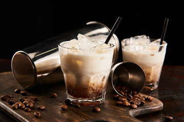 white russian cocktail in glasses with straws on wooden board with coffee grains and shaker...