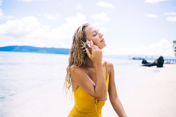 Young blonde with eyes closed sitting and listening to seashell