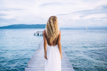 Fototapeta premium Seductive shapely female in light dress standing on pier