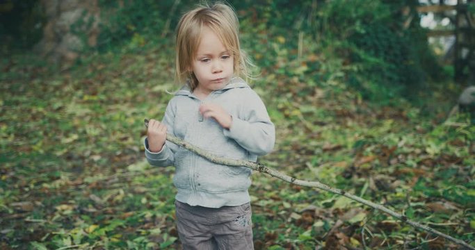 Little toddler walking in the woods with a big stick