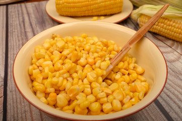 Grains of sweet corn in a plate with a wooden spoon and ears of corn on the table. Healthy diet. Fitness diet. For a sweet treat. Close up.