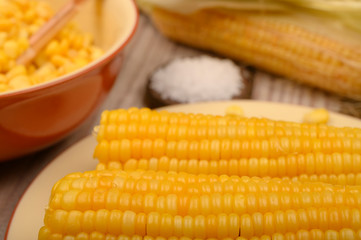 Grains of sweet corn in a plate with a wooden spoon, coarse salt and ears of corn on the table. Healthy diet. Fitness diet. For a sweet treat. Close up.