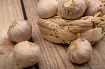 A few heads of young garlic in a wicker basket on a wooden background. Autumn harvest. Modern agriculture. Close up.