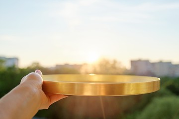 Round golden brass metal tray in womans hands, background sunset