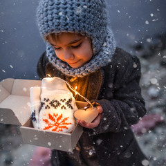 Girl in knitted grey hat opening a gift box with warm gloves