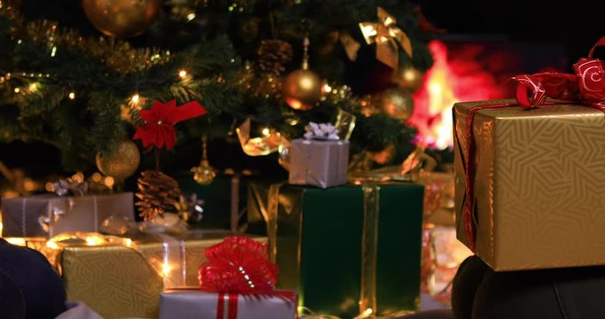 Woman hands giving a gift in front of Christmas tree and fireplace. Giving for Christmas atmosphere. Dolly shot 4k