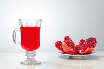 Pomegranate, red tea on a gray background, open ripe pomegranate on a white saucer