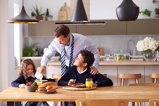 Children Wearing School Uniform Eating Breakfast As Father Gets Ready For Work