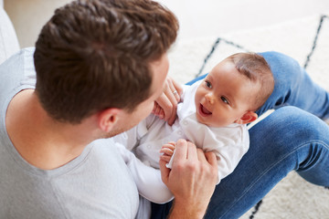 Baby Daughter Lying On Fathers Lap As He Plays Game With Her At Home