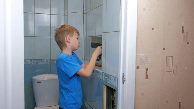Child boy makes renovation repair at home, he removes tiles from wall in toilet using tools spatula. Construction works at home. Children labour. Little repairer helping to adults.