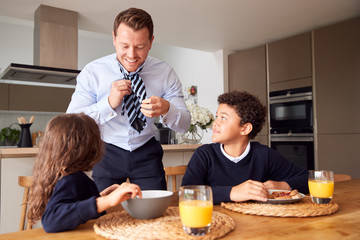 Fototapeta na wymiar Children Eating Breakfast Before School As Father Get Ready For Work In Office