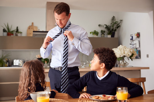 Children Eating Breakfast Before School As Father Get Ready For Work In Office