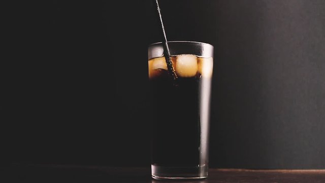 Someone drinking cola from straw in glass with ice cubes, dark background