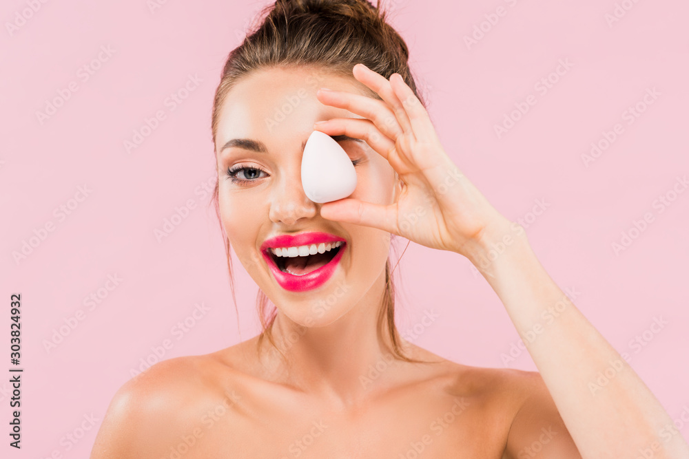 Wall mural happy naked beautiful woman with pink lips and open mouth holding makeup sponge isolated on pink