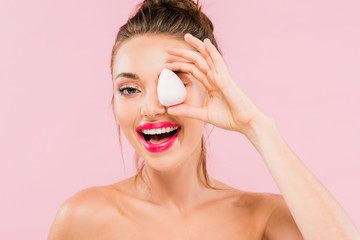 happy naked beautiful woman with pink lips and open mouth holding makeup sponge isolated on pink