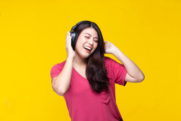 Portrait of beautiful young asian woman dancing and listening to music having fun in summer on yellow background.