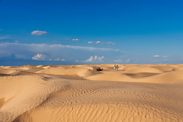 the sands and dunes of the Sahara desert, with camels and people sitting on camels