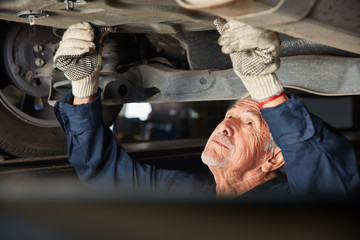 Obraz na płótnie Canvas KFZ Mechaniker bei Auto Reparatur unter dem Auto