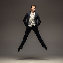 Fototapeta na wymiar Man in casual office style clothes jumping and dancing isolated on grey background. Art, motion, action, flexibility, inspiration concept. Flexible caucasian ballet dancer, weightless jumps.