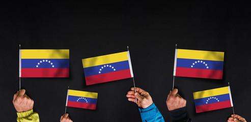 Fototapeta na wymiar Hands holds flags of Venezuela on dark background
