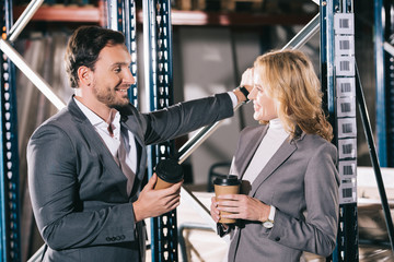 two smiling businesspeople talking in warehouse while holding disposable cups