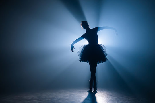 Ballerina In Black Tutu Dress Dancing On Stage With Magic Blue Light And Smoke. Silhouette Of Young Attractive Dancer In Ballet Shoes Pointe Performing In Dark. Copy Space.