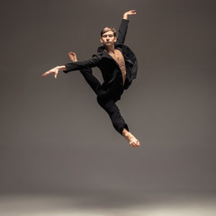 Man in casual office style clothes jumping and dancing isolated on grey background. Art, motion,...
