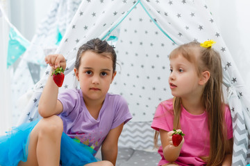 two little girls eat strawberries at home near wigwam tent © Angelov