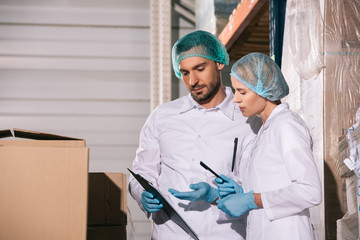 Fototapeta na wymiar two storekeepers in white coats and hairnets looking at clipboard in warehouse