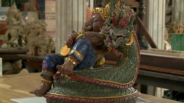 Close up of a shiny, painted, ceramic statue of Ganesh, seated on a dragon