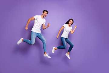 Fototapeta na wymiar Turned full length body size photo of cute pretty nice couple of two people running jumping for sales in t-shirt white jeans denim footwear isolated violet pastel color background