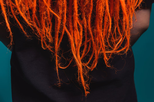 Dreadlocks orange red close-up. Braiding dreadlocks from natural hair. A girl with fiery red dreadlocks back view.