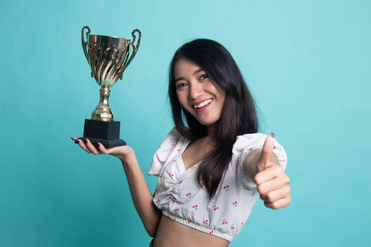Successful young asian woman holding a trophy show thumb up