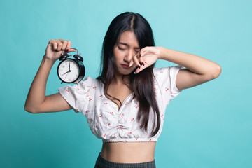 Sleepy young Asian woman with a clock in the morning.