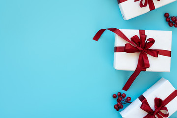 Gift boxes wrapped white paper and red ribbon decorated berries on blue background. Top view. Flat lay.  Christmas and New Year holidays concept