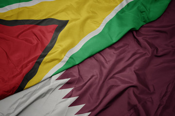 waving colorful flag of qatar and national flag of guyana.