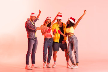 excited men and multicultural girls in santa hats holding plastic cups on pink
