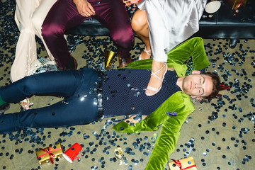 Fototapeta na wymiar handsome and drunk man sleeping on floor near friends and confetti after party