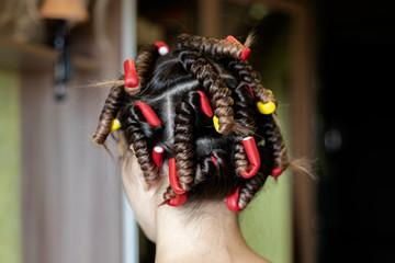 A woman with curlers on her head. Curlers on the girl's head red and yellow close-up. Rear view