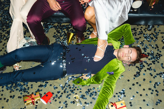 handsome and drunk man sleeping on floor near friends and confetti after party
