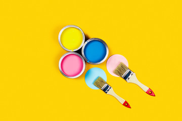 Renovation concept. Yellow background with three paint jars and two brushes. Flat lay, top view, copy space.