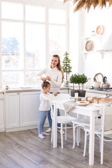 Mother and daughter spending time together at light Christmas kitchen.